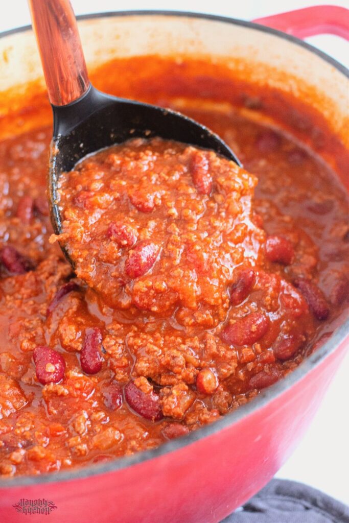 chili close up with ladle in red dutch oven