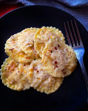 plant based ravioli in herb infused white sauce with fork and black plate.