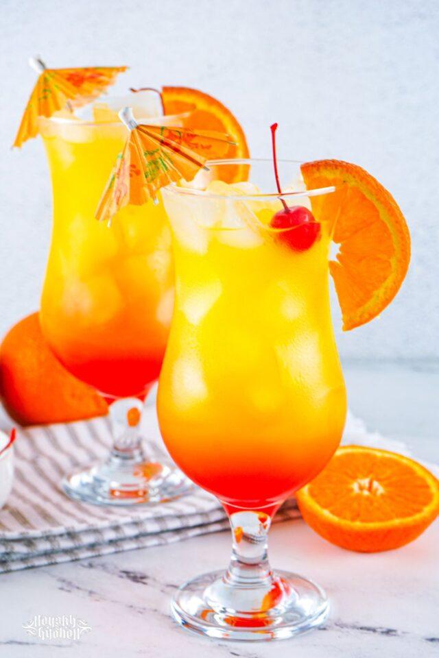 Two Tequila Sunrise Cocktail glasses with umbrellas.