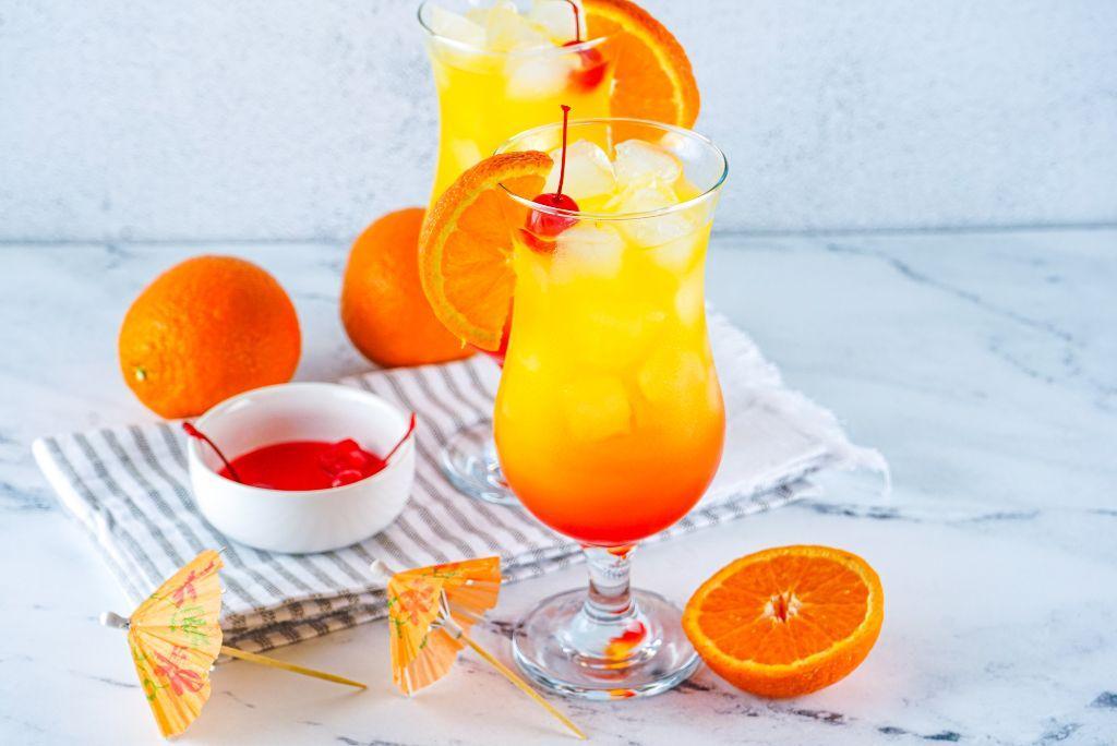 Two Tequila Sunrise Cocktail glasses with oranges and cherries.