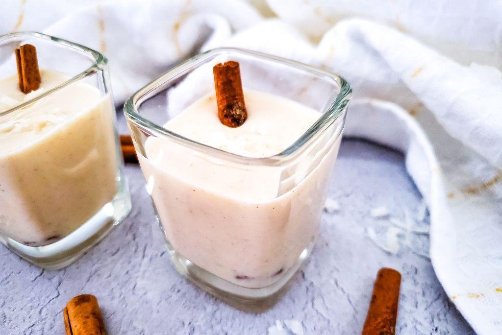 Coquito in shot glasses with cinnamon sticks.