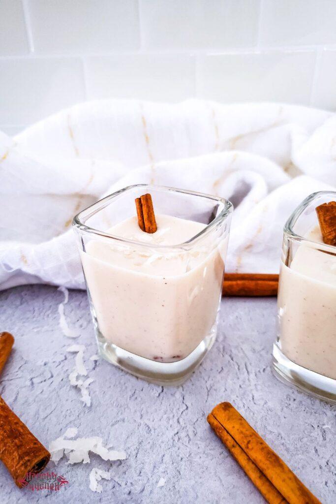 Coquito in a shot glass with cinnamon sticks and coconut flakes.