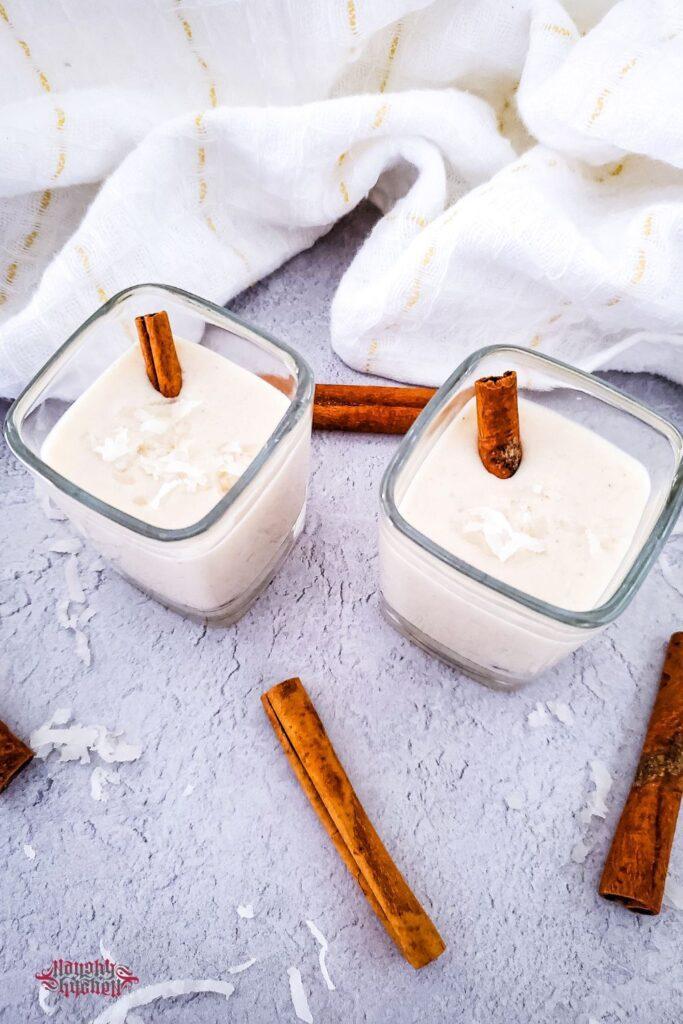 Coquito in shot glasses with cinnamon sticks above.