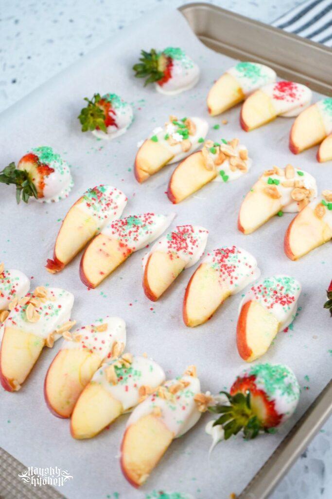 Holiday Dipped Apples and Strawberries on a baking sheet.