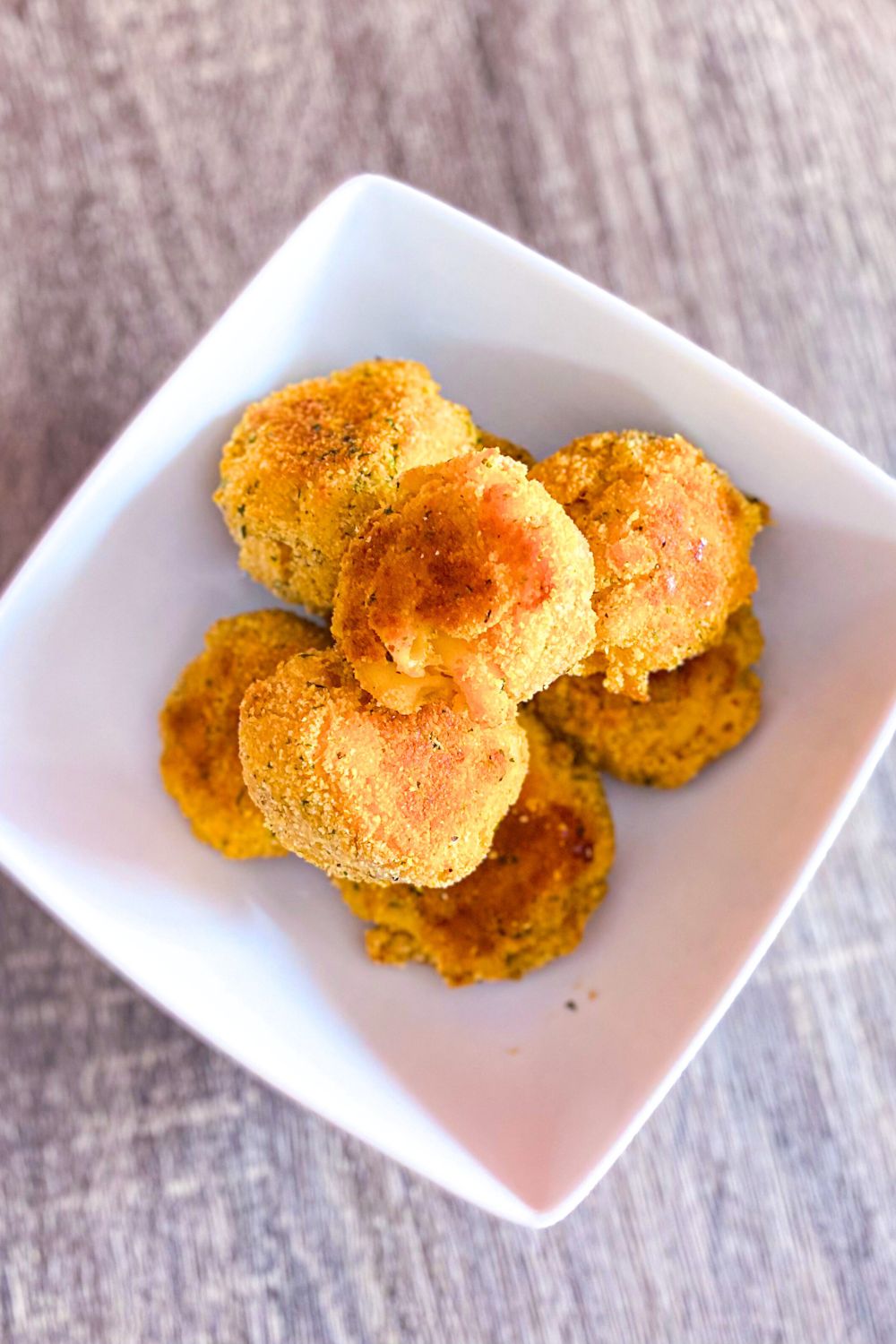 Mac and cheese bites in a white bowl over table top.