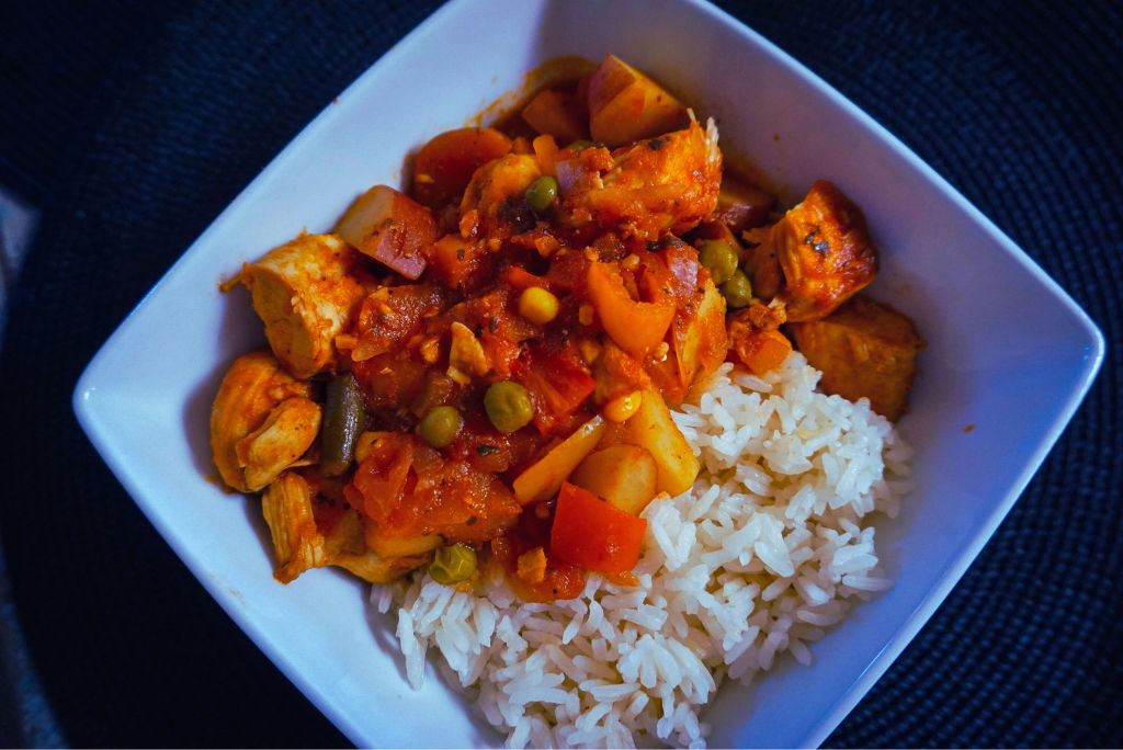 Chicken Afritada in a white bowl with rice.