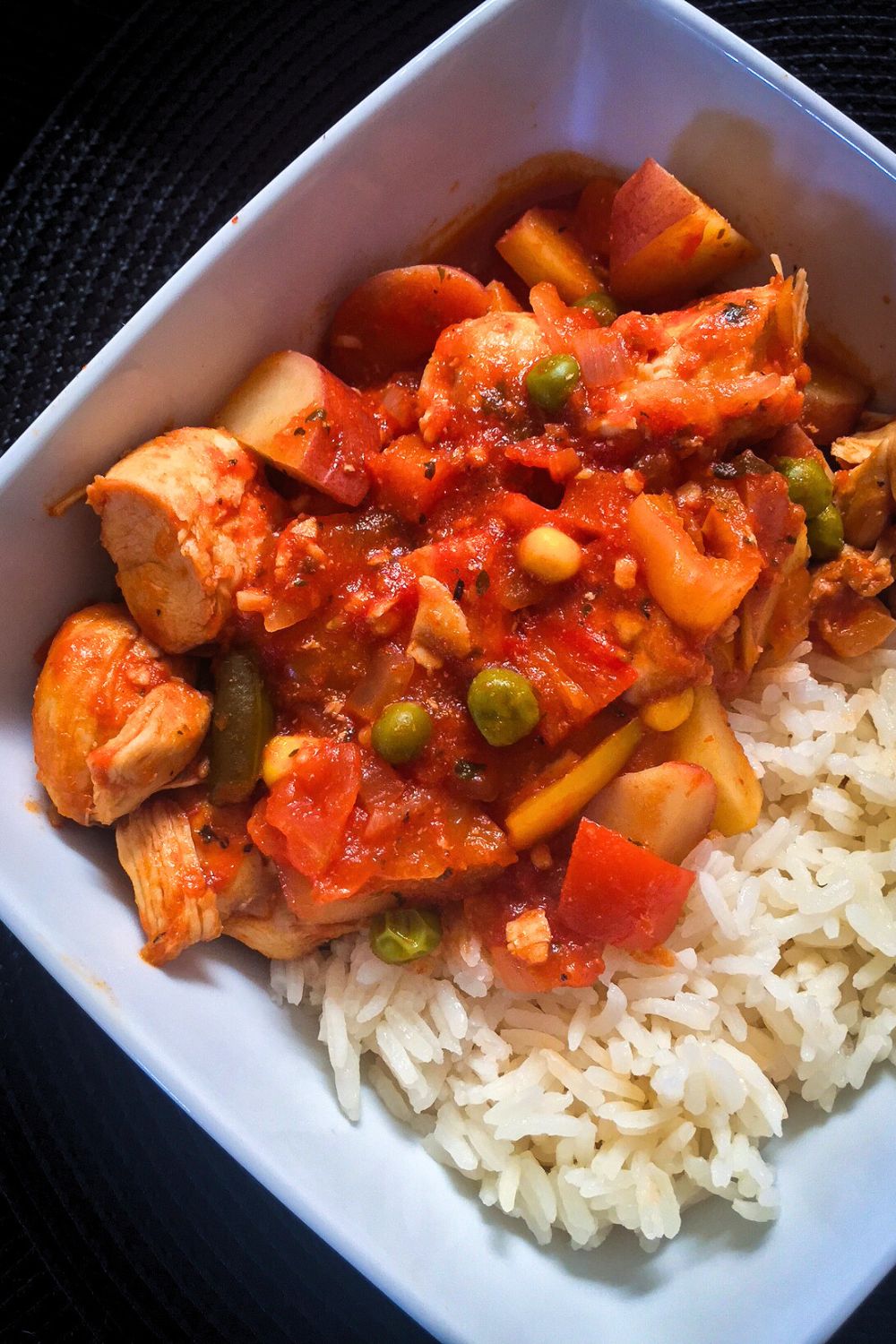 Chicken Afritada in a white bowl with jasmin rice.