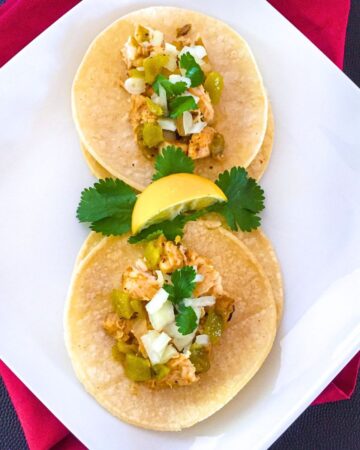 Overview of street tacos garnished with cilantro and onions served with lemon wedge and hatch chiles.