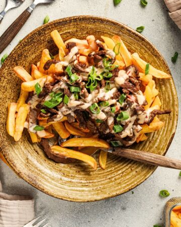 Golden crispy Korean loaded fries topped with seasoned beef strips, creamy spicy mayo drizzle, and fresh green onions on a plate