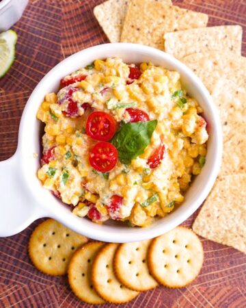 Overview of creamy white corn dip with colorful cherry tomatoes and fresh green basil in a bowl
